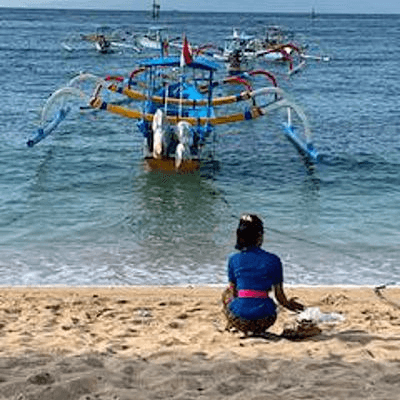 Bateaux traditionnels et femme déposant des offrandes sur la plage à Bali