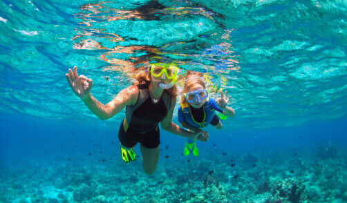 Mother, kid in snorkeling mask dive underwater with tropical fis
