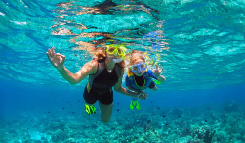 Mother, kid in snorkeling mask dive underwater with tropical fis